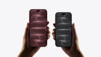Two hands holding two iPhones side by side against a light gray background. The phone on the left has a dark rose pink front, and the phone on the right has a dark gray front.
