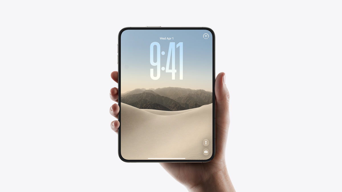 A hand holding a smartphone with a large screen displaying a mountain and dune wallpaper, set against a clean white background.